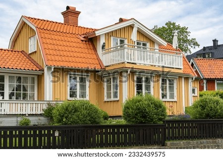 Old wooden yellow house with big balcony. Typical Swedish house surrounded by palisade fence. Beautiful wooden fence of natural wood is not painted. Ecological design. Royalty-Free Stock Photo #2332439575