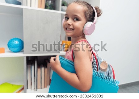 happy little girl equipped with backpack, folder and headphones ready for the start of the new school year; back to school Royalty-Free Stock Photo #2332451301