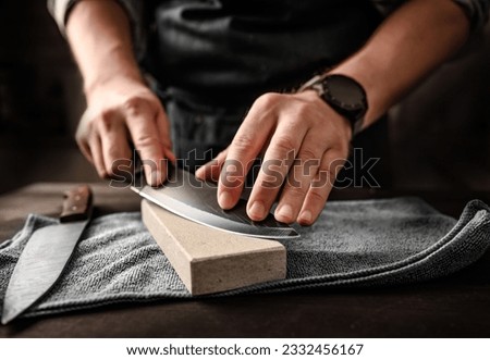 Man sharpening knifes with special stone tool, closeup view Royalty-Free Stock Photo #2332456167