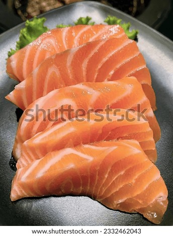 a photography of a plate of salmon slices on a table, there are salmon slices on a plate with lettuce and sauce.