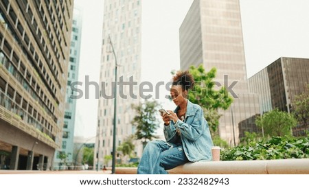 Girl with ponytail wearing denim jacket leaving voice message on mobile phone against modern city background. Royalty-Free Stock Photo #2332482943