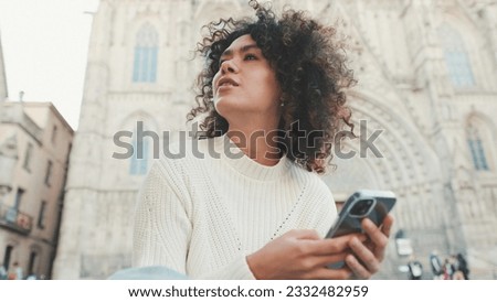 Young woman looks around. Happy girl uses mobile phone on old city background Royalty-Free Stock Photo #2332482959