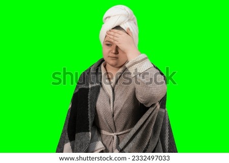 A girl with symptoms of a cold holds her head on a green background (chroma key). Headache, high body temperature. The concept of medicine, pharmacy, healthcare and home treatment