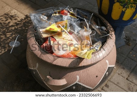 A large pot filled with trash sits on a sidewalk.