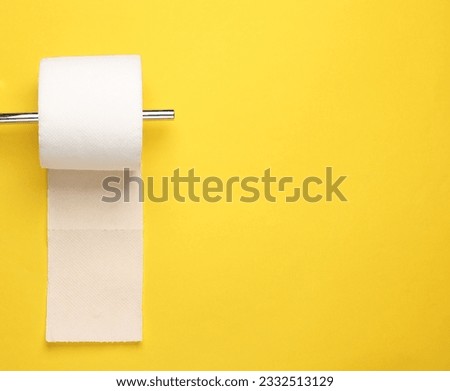 Metal Toilet paper holder with a roll of toilet paper on a yellow wall. minimalistic photo Royalty-Free Stock Photo #2332513129