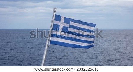 Greece sign symbol of leading shipping power in the world. Greek flag on flagpole waving over rippled sea water. Cloudy sky background.