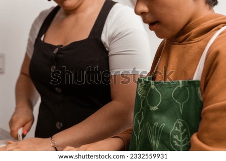 The brown-haired boy is wearing a green apron and cooking with his mother at home-they are in a sunny kitchen-Pictures of family members cooking-Cooking with the family-.