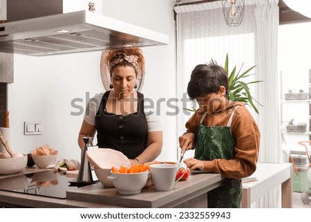 10-year-old brown-haired boy cuts a tomato and cooks with his mother-they are in a sunny kitchen-Pictures of family cooking-Cooking with the family
