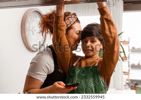 A mom cooking at home and having fun with her 10-year-old brown-haired son-She's teaching him a recipe on her cell phone-they're in a sunny kitchen-Pictures of family members cooking-Family Cooking