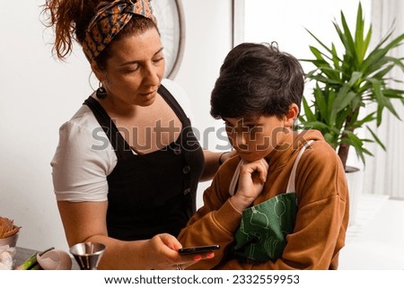 A mom cooking at home with her brown-haired, 10-year-old son-She's teaching him a recipe on her cell phone-they're in a sunny kitchen-Pictures of family members cooking-Family cooking.