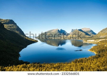 Serene mountain lake nestled amidst lush green trees and surrounded by majestic mountains.Crystal-clear blue water reflects clear sky with few fluffy clouds Royalty-Free Stock Photo #2332566831