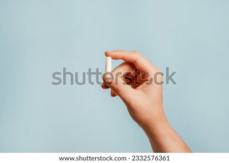 White pill in female hand on blue background, Taking Your Medication Royalty-Free Stock Photo #2332576361