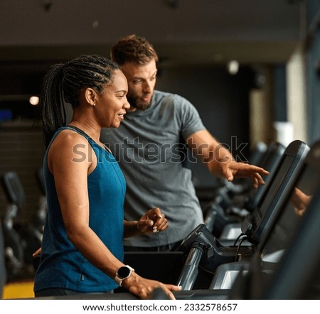 Portrait of a young black woman and white man coach or trainer exercising in a gym, running using  thereadmill machine equipment, healthy lifestyle and cardio exercise at fitness club concepts Royalty-Free Stock Photo #2332578657