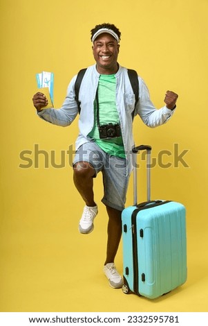 The traveler, a dark-skinned man in denim shorts and a cap, holds a plane ticket and passport, makes a gesture of victory. African-American tourist rejoices in upcoming summer vacation Royalty-Free Stock Photo #2332595781