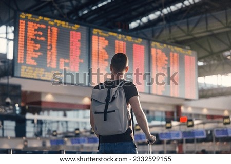 Traveling by airplane. Man walking with backpack and suitcase walking through airport terminal and looking at departure information.
 Royalty-Free Stock Photo #2332599155