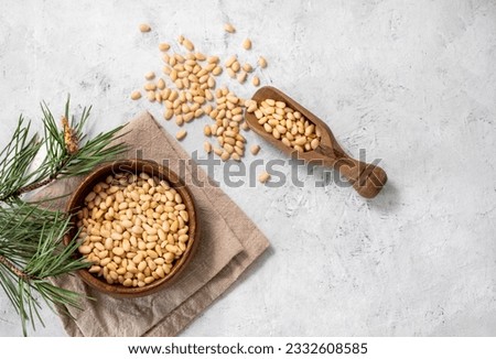 Pine nuts in a bowl  on napkin and scattered on a white texture background with branches of pine needles. The concept of natural, organic and healthy superfoods and snacks.  Top view and copy space. Royalty-Free Stock Photo #2332608585