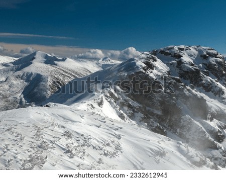 Winter's majesty unfolds atop a high mountain peak. Snow-draped landscapes stretch endlessly, dotted with delicate pine trees. Clouds swirl overhead, adding an ethereal touch to this serene.