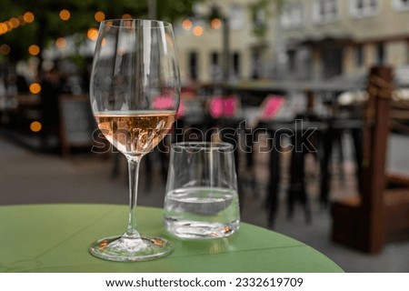 Glass of refreshing rose wine and a glass of water on the green table of a city cafe terrace during warm summer evening. Street in bokeh. Royalty-Free Stock Photo #2332619709