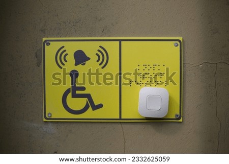 Yellow plate with image of disabled person in wheelchair and call button. Disabled person sign and panic button for help in front of the entrance to the building near the stairs, braille text