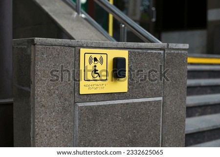 Yellow plate with image of disabled person in wheelchair and call button. Disabled person sign and panic button for help in front of the entrance to the building near the stairs, braille text