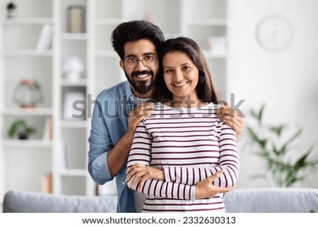 Portrait of cheerful young indian lovers enjoying time together at home, happy hindu man and woman posing in living room, embracing and smiling at camera, copy space. Love, family, relationship