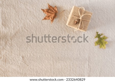 Autumn composition with autumn dry leaves, a gift wrapped in kraft paper, laid out in a corner on a rustic linen fabric background. Flat lay, top view, copy space