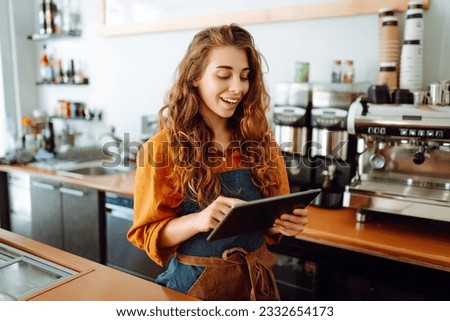 Beautiful woman owner stands behind the counter of a coffee shop. A barista with a digital tablet takes an order. Business concept. Takeaway food. Royalty-Free Stock Photo #2332654173