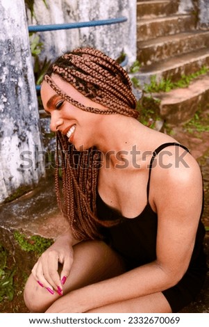 Portrait of a transgender girl with braids smiling at the sun wearing a floral dress . Taking direct sun light