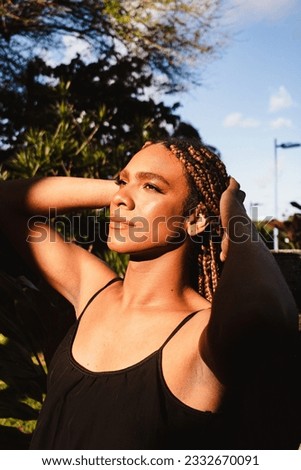 Portrait of a transgender girl with braids smiling at the sun wearing a floral dress . Taking direct sun light