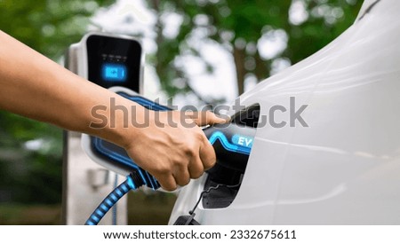 Hand insert EV charger and recharge electric car from charging station on nature and travel concept background. Technological advancement of alternative energy sustainability and EV car. Peruse