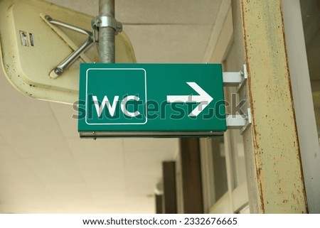 A water closet bathroom sign in Switzerland during the day directing people to the right for the entrance.