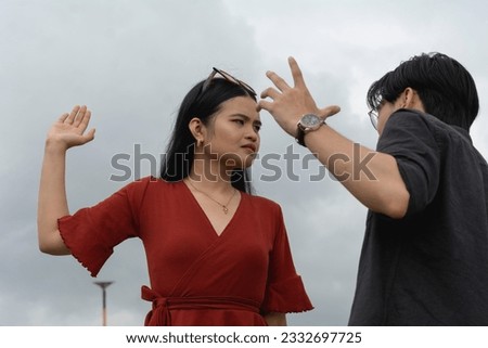 An annoyed woman threatens to slap her submissive and meek boyfriend during an argument. Outdoor scene. Royalty-Free Stock Photo #2332697725