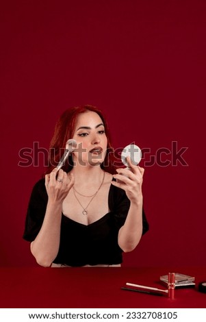 Woman applying makeup on her face against a colored isolated background.