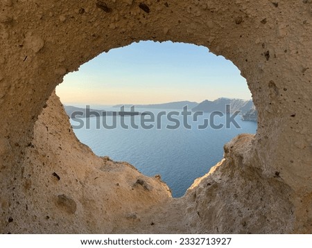 Sunset view through a natural window created by a hole in sandstone overlooking the ocean in the Greek islands