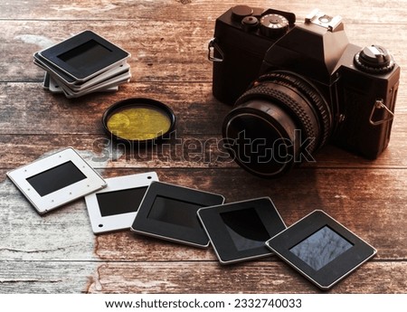 Vintage camera with yellow filter and slides on wooden background. Retro style technology