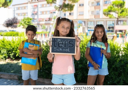 Group Of School Kids With Board In The Park Back To School. Group Of Happy Young Best Friends Smiling On The First Day Of School. Education.