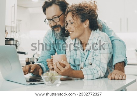 Portrait of man and woman at home enjoyng surf the web together with wireless laptop. White modern kitchen apartment in background. Concept of adult couple living together with happiness. Relationship Royalty-Free Stock Photo #2332772327