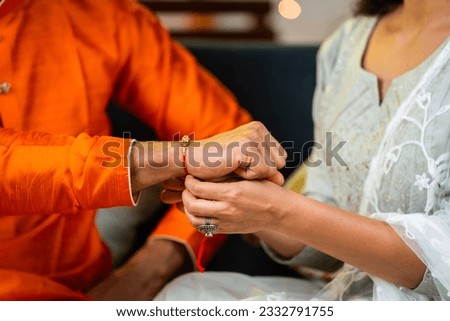 Close up shot of indian girl tying rakhi to brother hand during raksha bandhan festival at home - concept of indian culture, relationship and occasion