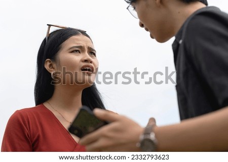 A man demands an explanation from his cheating partner after catching his unfaithful girlfriend's flirty chat messages with another guy on her phone. Pointing to the cellphone. Royalty-Free Stock Photo #2332793623