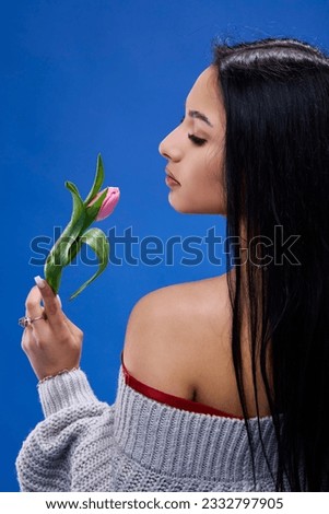 A beautiful young woman with tulips in her hand posing in the studio on a blue background