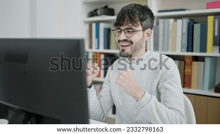 Young hispanic man using laptop celebrating at university classroom