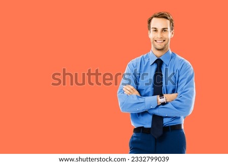 Portrait photo of happy smiling businessman in blue cloth, standing in crossed arm pose, isolated over bright vivid orange color background. Confident business man at studio image.