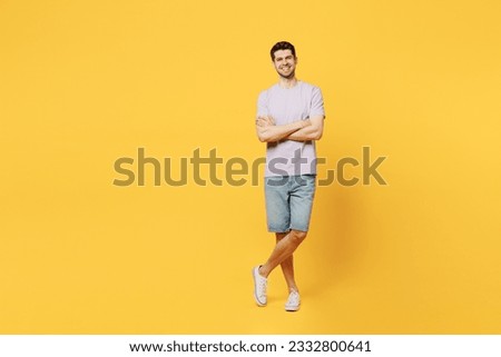 Full body young cheerful happy fun smiling man he wear light purple t-shirt casual clothes look camera hold hands crossed folded isolated on plain yellow background studio portrait. Lifestyle concept