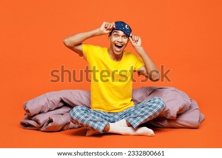 Full body surprised happy young man wear pyjamas jam take off sleep eye mask sit with duvet blanket rest relax at home isolated on plain orange background studio portrait. Good mood night nap concept Royalty-Free Stock Photo #2332800661