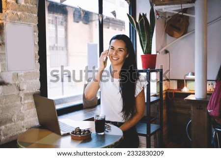 Portrait of happy female programmer with laptop enjoying cellphone conversation for discussing graphic design, successful woman with netbook phoning via mobile application and smiling at camera