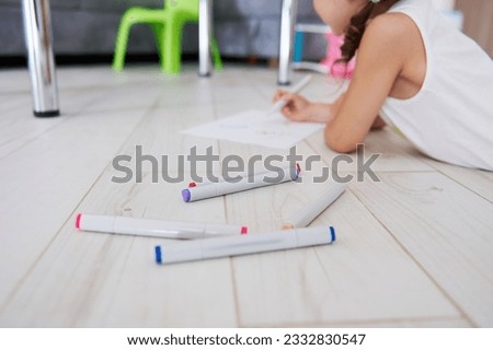 Selective focus on felt-tip-pens or watercolor markers on floor on the background of a blurred little girl, drawing picture at home. School stationery. Art. Painting. Creative hobby. People. Lifestyle