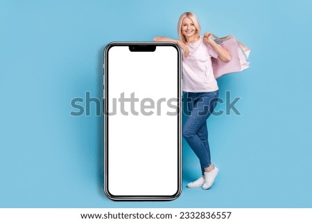 Full size photo of optimistic woman white t-shirt sneakers lean on display smartphone online shopping isolated on blue color background