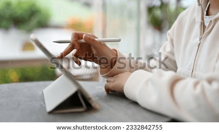 Close-up image of an Asian female freelancer using her digital tablet while siting in a coffee shop on the weekend. digital nomad, remote working