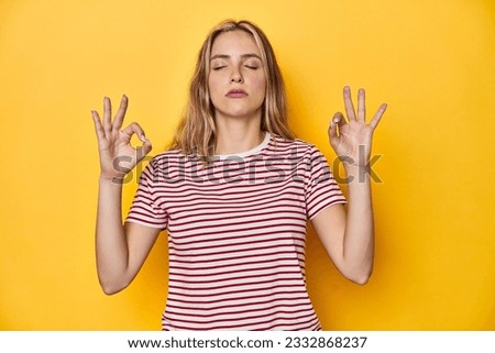 Young blonde Caucasian woman in a red striped t-shirt on a yellow background, relaxes after hard working day, she is performing yoga.
