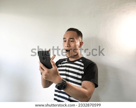 Smile and happy, sad, and amazed face of Young Asian man when playing gameand watching a movie on cell phone in hand. Isolated white background and stripe shirt